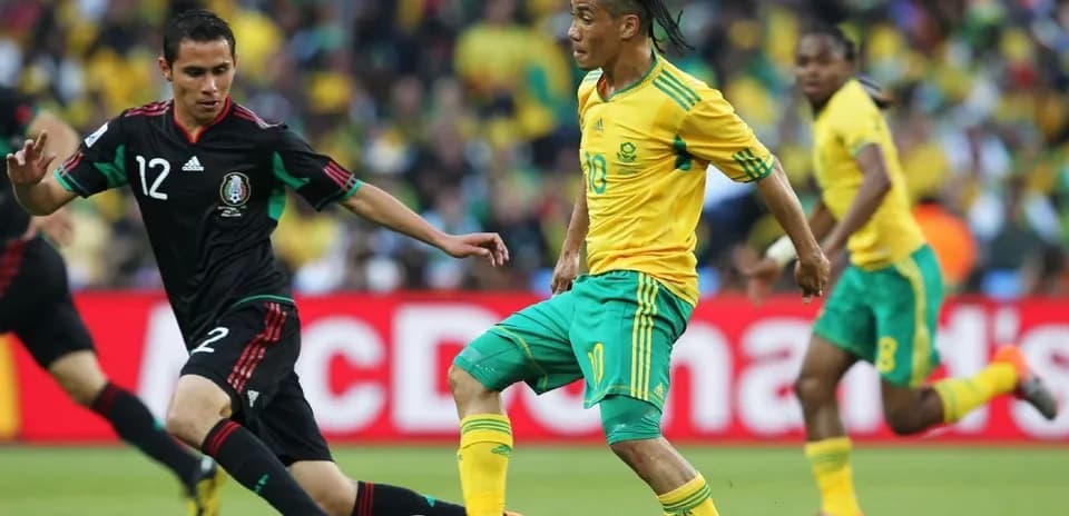 Jugador sudafricano driblando a jugador mexicano en partido