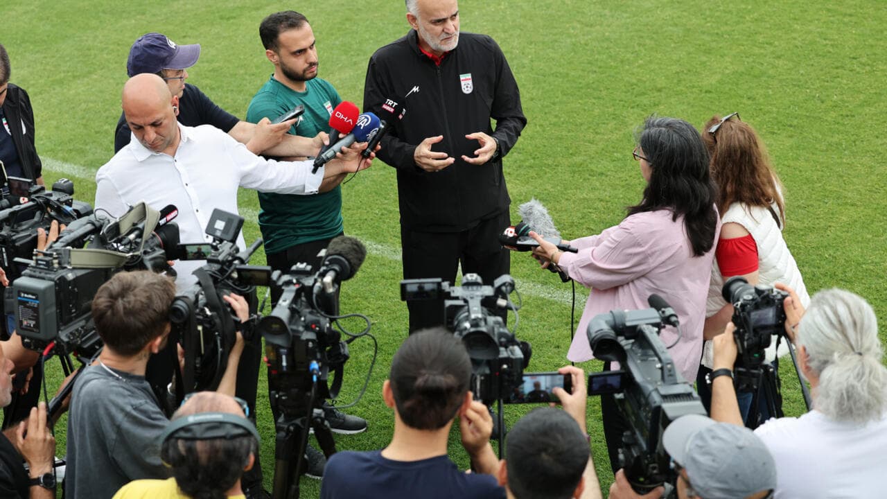 Entrenador dando una conferencia de prensa rodeado de periodistas