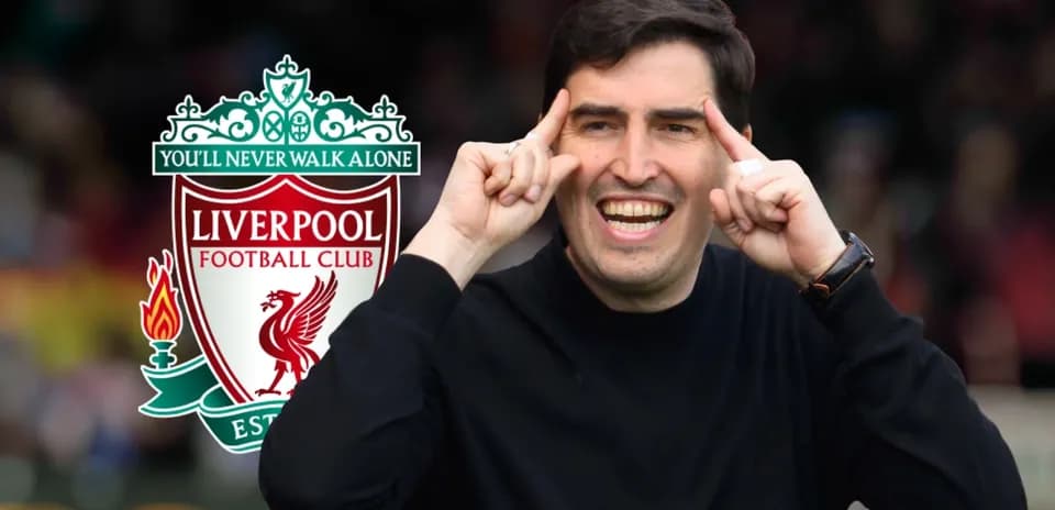Entrenador señalando con una sonrisa junto al logo de Liverpool