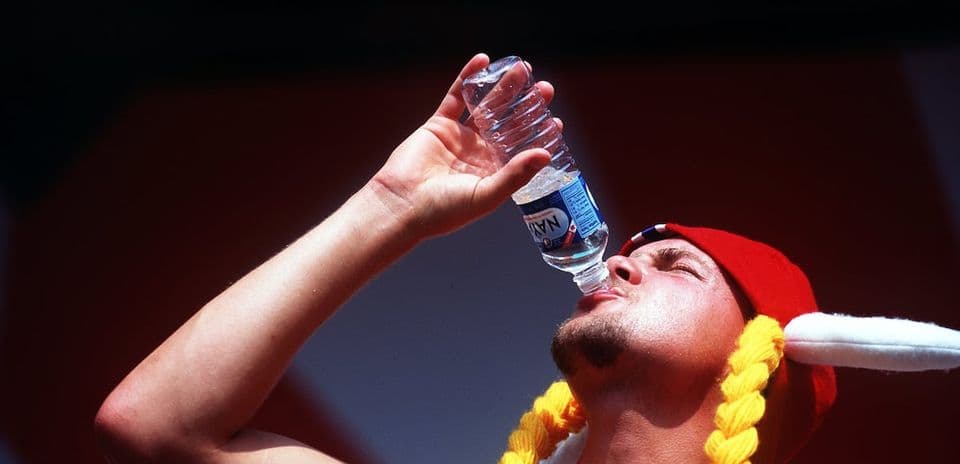 Hombre bebiendo agua de una botella con gorro rojo Hombre bebiendo agua de una botella con gorro rojo