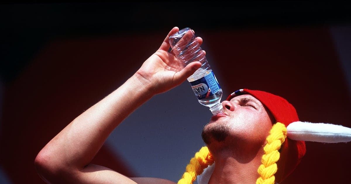 Hombre bebiendo agua de una botella con gorro rojo Hombre bebiendo agua de una botella con gorro rojo